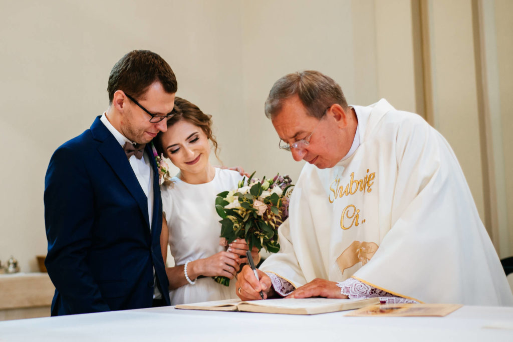 Przebieg ślubu kościelnego - podpisanie dokumentów. Zdjecie wykonanie w kościele w Iławie, podczas ślubu konkordatowego. Ksiąc podpisuje dokumenty, chwilę po podpisaniu ich przez Parę Młodą. Od teraz są małżeństwem nie tylko przed Bogiem, ale także przed państwem.