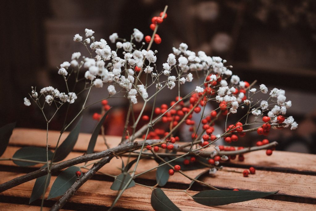 zimowe dekoracje sali weselnej - biała gipsówka, gałązki z czerwonymi owocami, zielony eukaliptus i dużo brązów w kolorze drewna